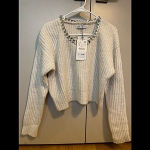 White sweater. Silver chain detail on collar.